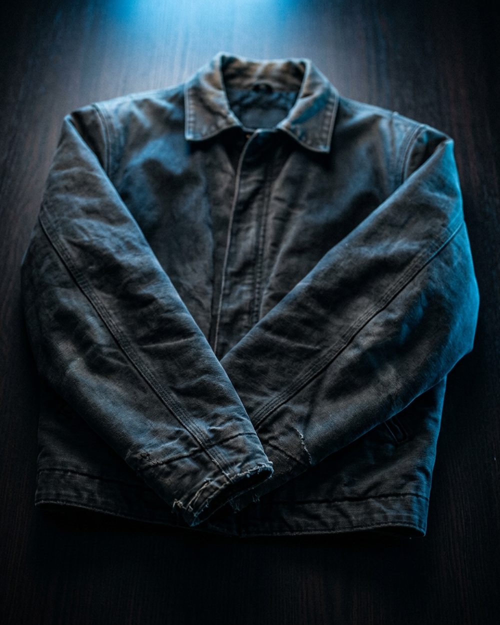 A used jacket laid flat on a dark desk, lit by a phone screen during a scan