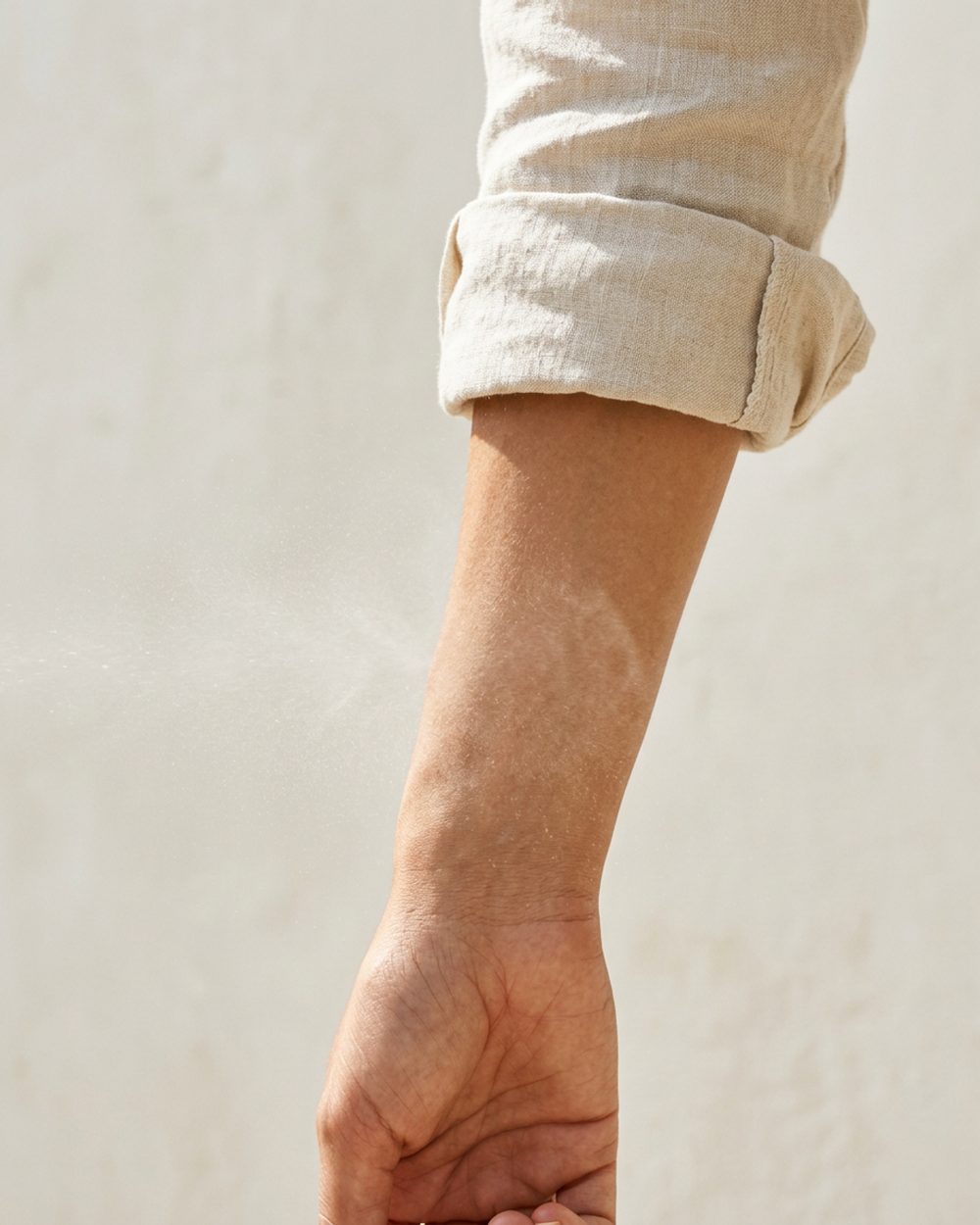 A wrist held in sunlight while a WHIT3 fragrance is sprayed onto the skin