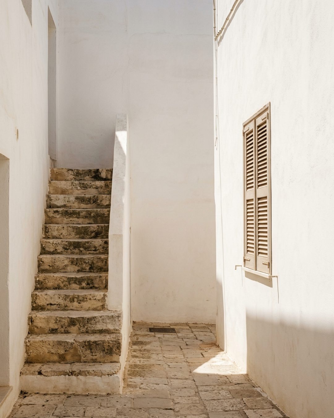 A sunlit lime-wash wall with stone steps rising beside it in hard noon light