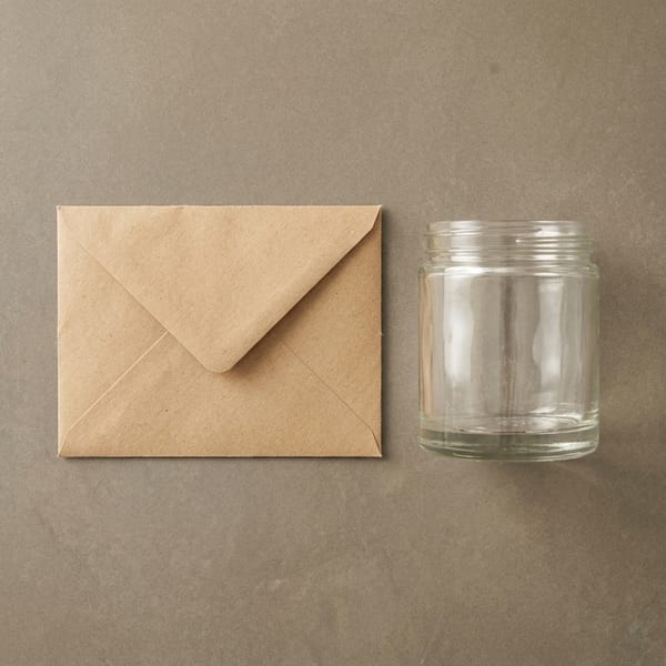A folded kraft return envelope beside an empty candle jar on a ceramic tray, ready to be sent back