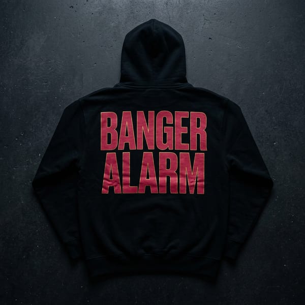 Banger Alarm Hoodie — back view showing BANGER ALARM bold block text and crimson graphic with gold foil accent on black heavyweight hoodie, flat-laid on concrete