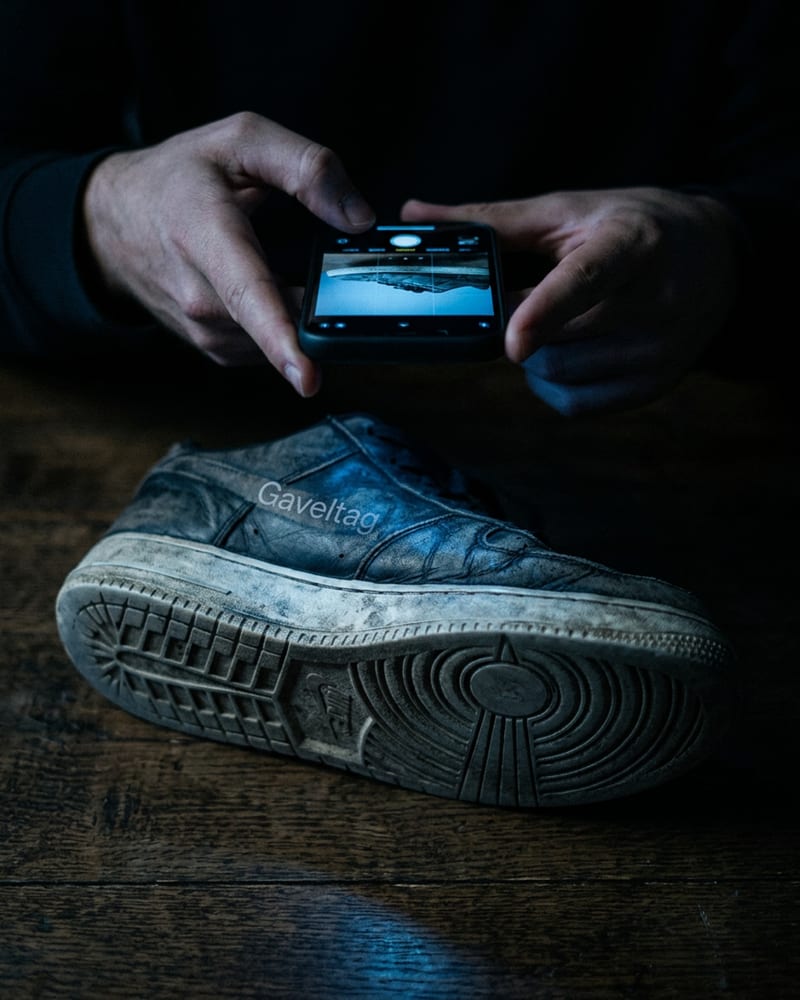 A reseller holding a phone over a used jacket on a dark desk, framing it for a scan