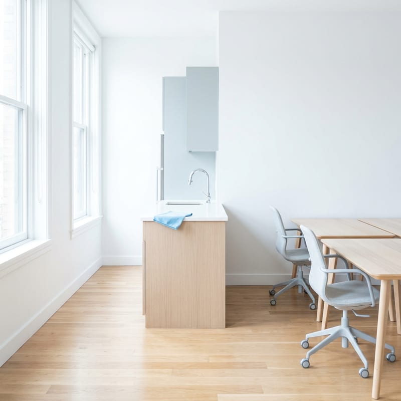 Small bright boutique office interior post-clean with wiped desks and natural morning light through large windows