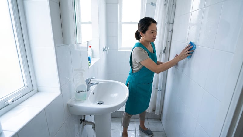 A female cleaner in a teal apron scrubbing the inside of an oven in a residential kitchen