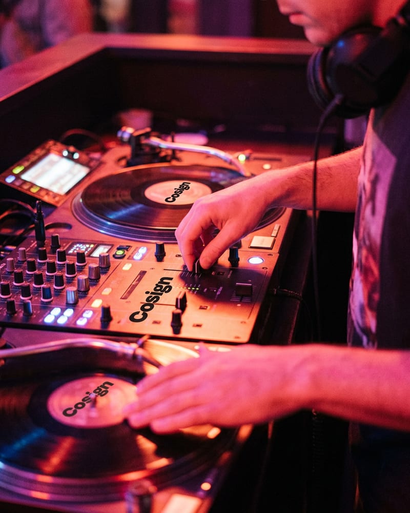 A DJ working a mixer in a booth lit by coloured gel lights
