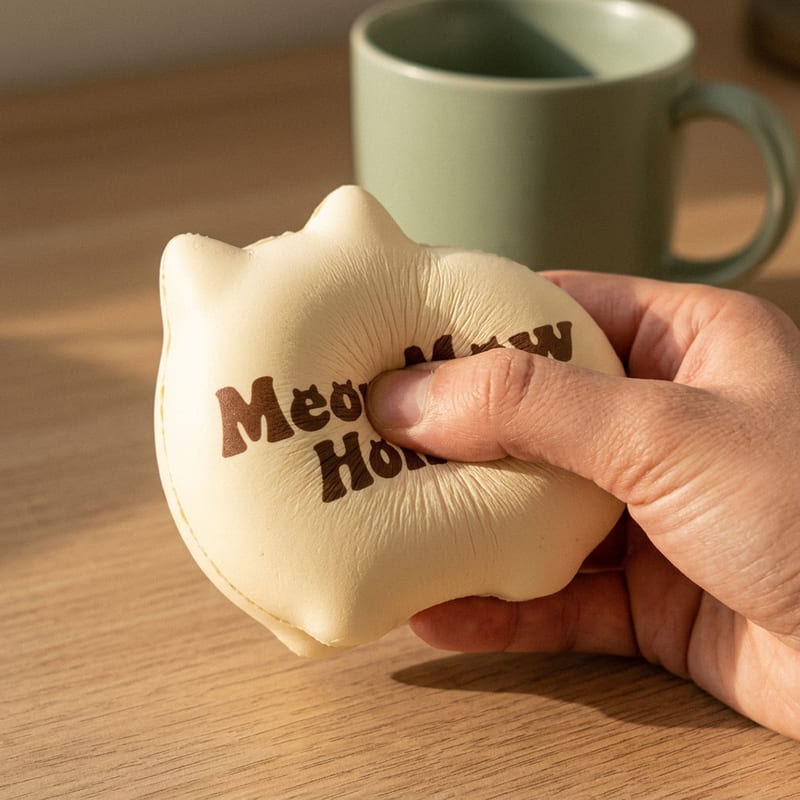 A palm-sized cream cat squishy mid-squeeze in an open hand, showing its springy foam texture