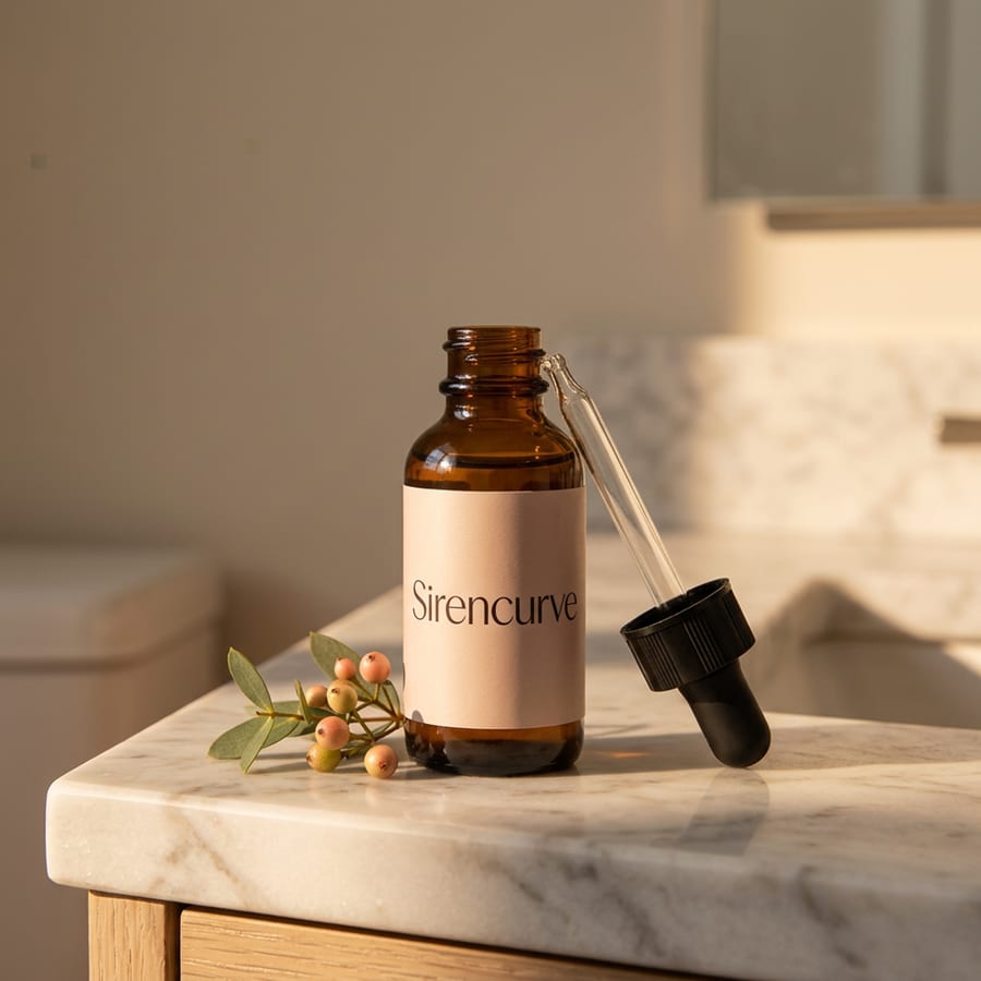 Sirencurve amber dropper bottle resting on marble beside botanicals in warm morning light
