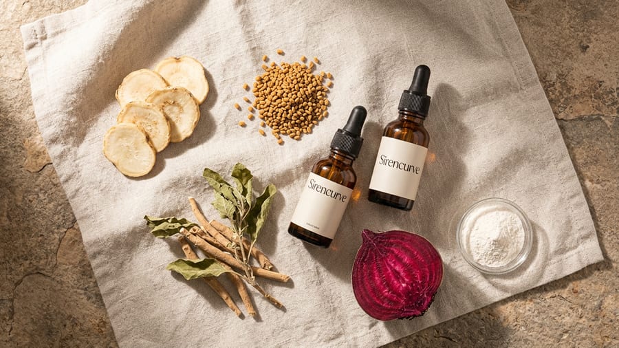 Amber dropper bottles resting beside raw maca root and botanicals on a stone surface, warm morning light