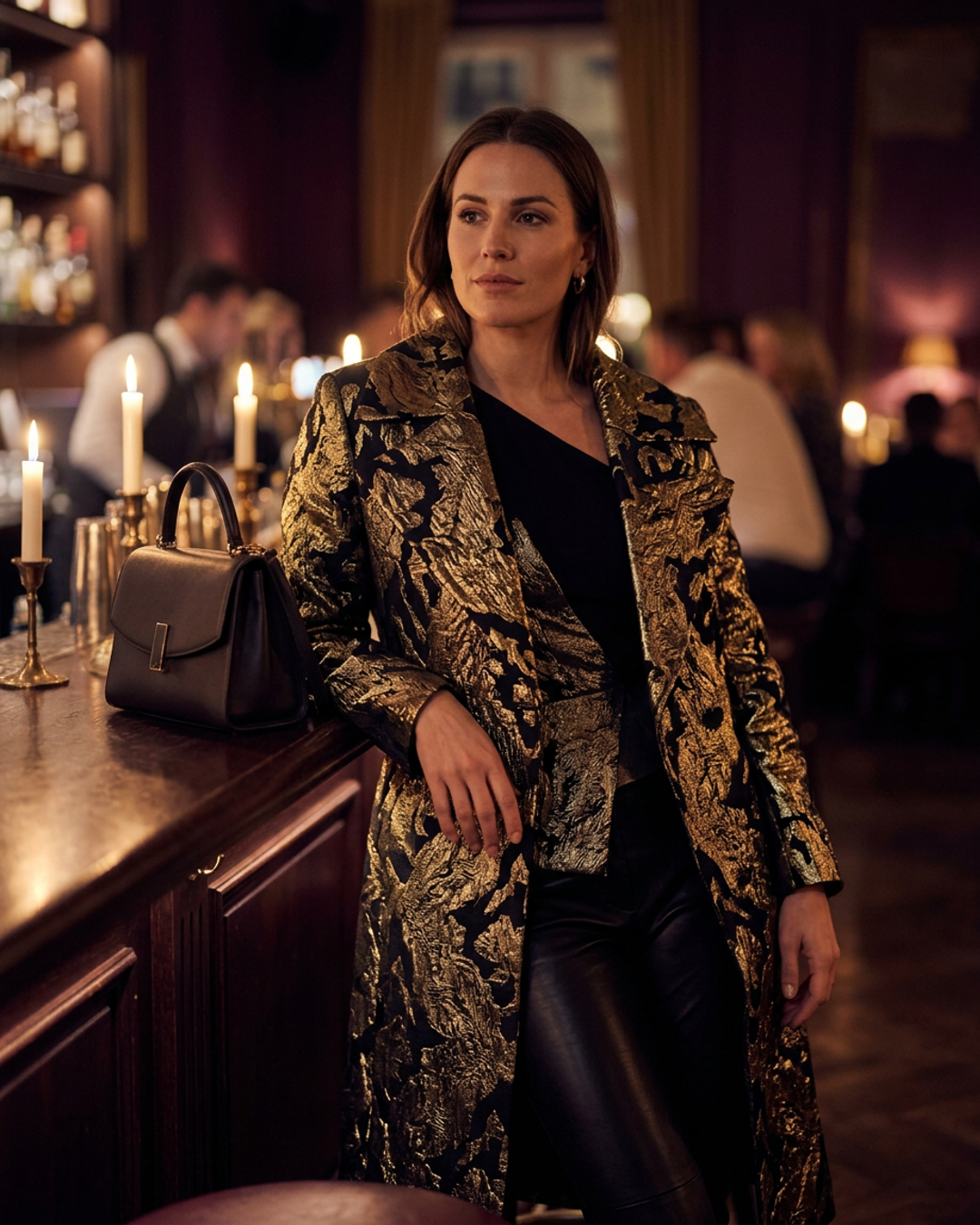 Woman wearing a Vixenne capsule statement piece in plum tones, standing in a warm-lit dressing room with champagne-gold fixtures